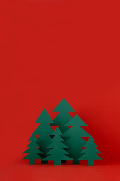 Stock image Christmas funny childish background with paper green spruce forest on saturated festive red backdrop in modern minimalist style, copy space, vertical. New year season mockup for design, greeting card.