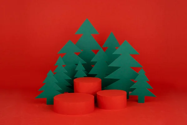 stock image Christmas background with three cylinder podiums and scene with 3d rendering for presentation gifts, cosmetics, goods in red color with green spruce forest. New year template for advertising.