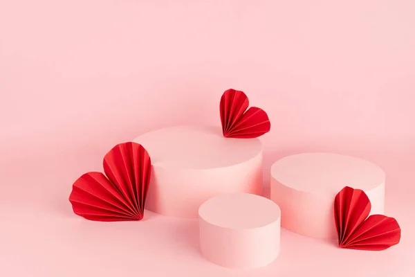Beautiful pink Valentines day scene mockup with three cylinder podiums, red ribbed paper hearts, copy space, top view. Love template for presentation cosmetic produce, goods, advertising, design.