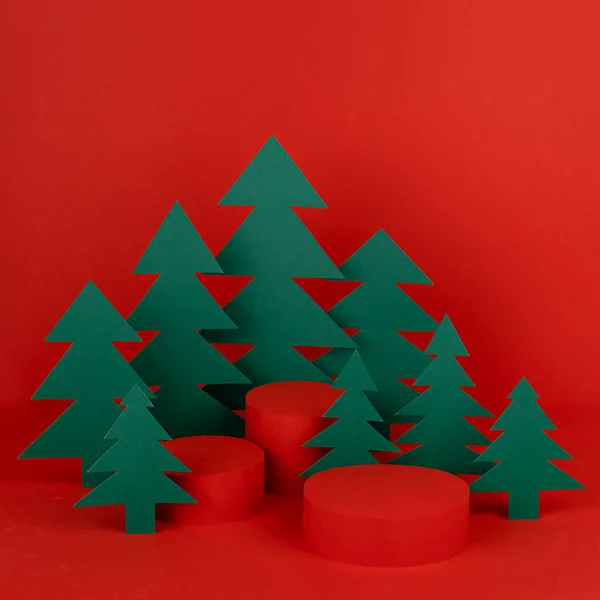 stock image Bright red New Year background with three red cylinder podiums mockup, green paper spruces as forest for presentation cosmetics, gifts, copy space, square. Christmas template for advertising, design.