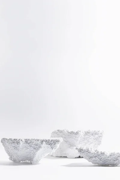 White scene with podiums of styrofoam as snowy icebergs mockup for presentation cosmetic produce, goods in bright light, shadows, closeup, vertical, copy space. Template stage in abstract art style.