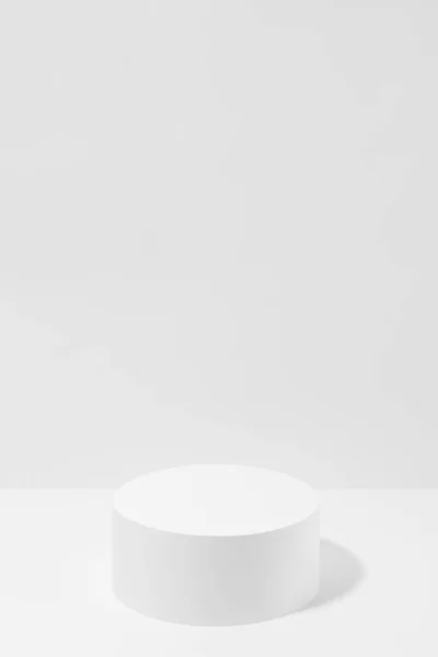 Abstract one white round podium for cosmetic products in hard light, mockup on white background, vertical. Scene for presentation products, gifts, goods, advertising, design, sale, display, showing.
