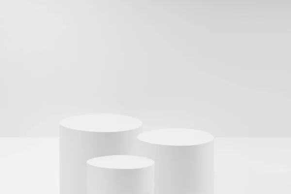 Abstract white stage with three white round podiums mockup for cosmetic products in hard light on white background. Scene for presentation cosmetic products, gifts, goods, advertising, design, sale.