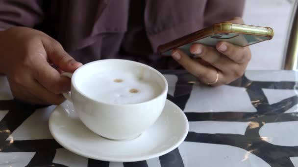 女性はコーヒーを飲んでテーブルの上でスマートフォンを使って — ストック動画