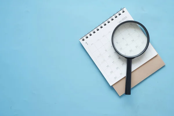 stock image top view of magnifying glass and a calendar on blue with copy space ,