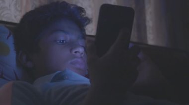  Genç çocuk geceleri akıllı telefon kullanarak kanepede oturuyor. .