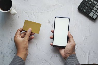 Adamın biri kredi kartını tutuyor ve online akıllı telefon alışverişi yapıyor. .