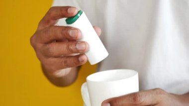 Genç adam çaya yapay tatlandırıcı koyuyor.