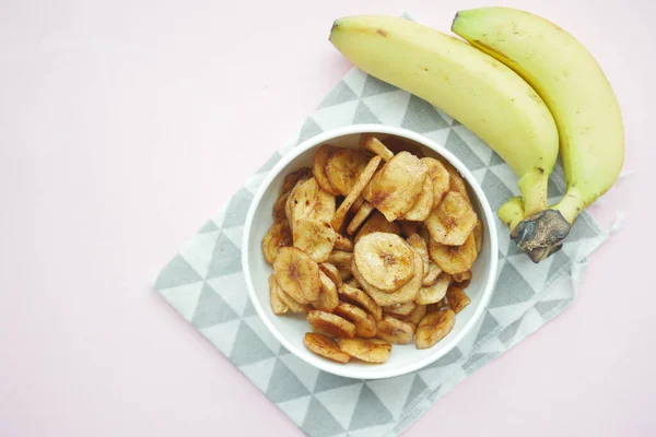 dry banana chips in a bowl on black tiles background .