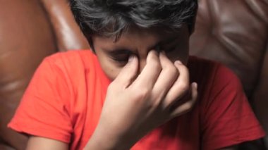 sad teenage boy covering his face sitting on sofa ,