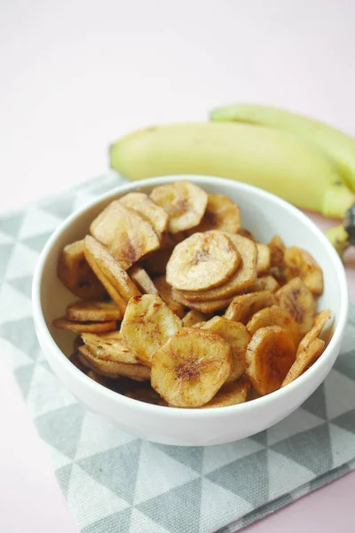 dry banana chips in a bowl on black tiles background .