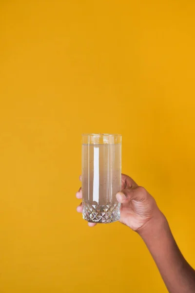 holding dirty glass of water against yellow background ,
