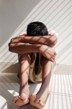 sad teenage boy covering his face sitting on floor .