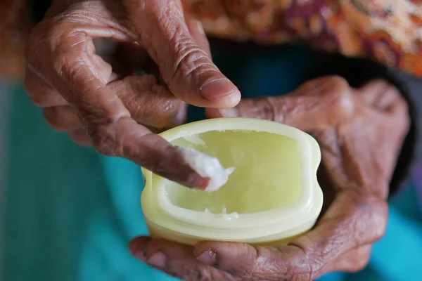 Stock image senior woman using petroleum jelly onto skin at home close up.