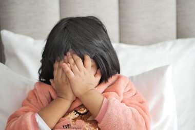 a upset child girl cover her face with hand .