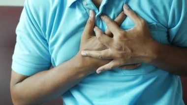 Genç adam kalp ağrısı çekiyor ve göğsünü eliyle tutuyor. .