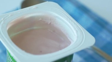 Plastik kabın içinde taze yoğurt ve masada kaşık. .