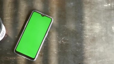 Yeşil ekranlı akıllı telefon ve masada bir fincan kahve. ,