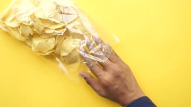 Elinde açık patates cipsi paketi vardı. ,