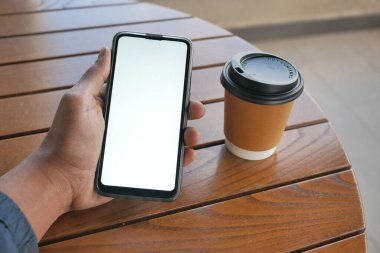 Masada beyaz ekranlı ve kağıt bardaklı akıllı telefon kullanarak. .