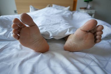  Genç kadın çıplak ayakla yatakta yatıyor.