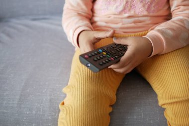  Çocuk kanepede otururken uzaktan kumandayı tutuyor. .