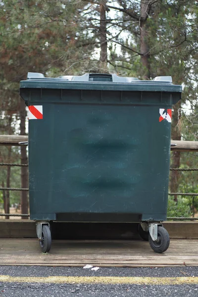 Metal green garbage can with wheels in countryside .