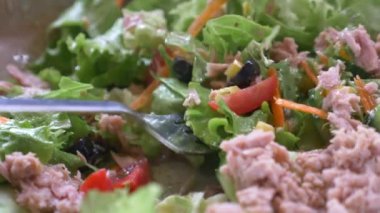 spoon pick tuna salad from a bowl on table .