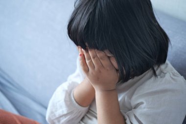 a upset child girl cover her face with hand .