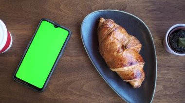 Kahve kruvasanı ve yeşil ekranlı akıllı telefon. 