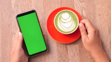 holding a cpu of coffee and using smart phone with green screen .
