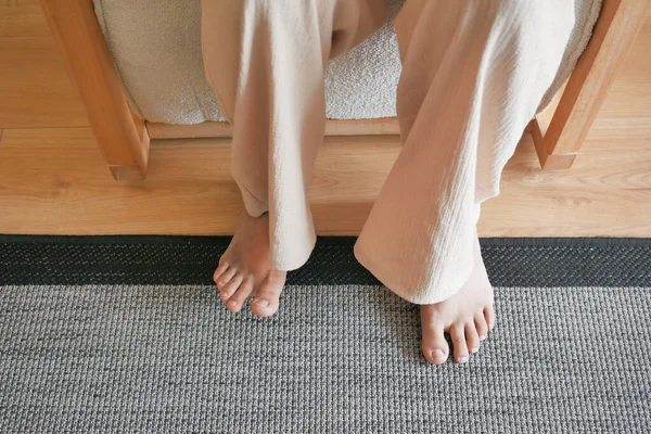 Woman sitting on sofa with feet on carpet at home