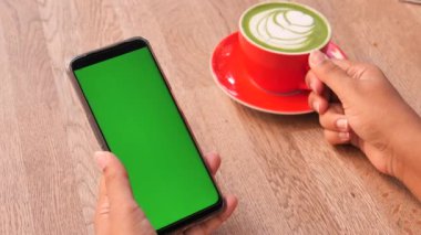 holding a cpu of coffee and using smart phone with green screen .