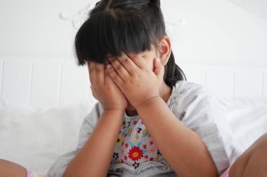 a upset child girl cover her face with hand .