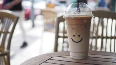 Plastik bir kapta soğuk kahve, üzerinde gülücük şekli tasarımı var. .