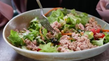 spoon pick tuna salad from a bowl on table .