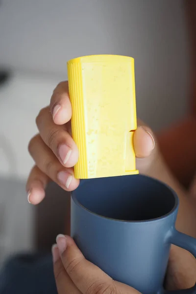 putting artificial sweetener in a coffee mug