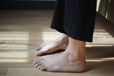 Evdeki halıda ayaklarıyla koltukta oturan kadın.