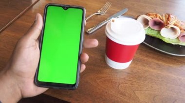 Yeşil ekranlı akıllı telefon ve masada bir fincan kahve. ,