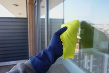 Mavi eldiven ile yeşil bez ile pencereyi temizleyin..