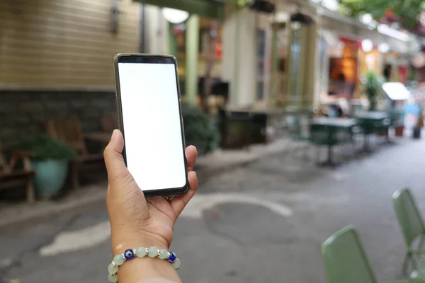holding smart phone with empty screen with blurred cafe street background.,