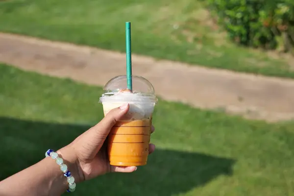 Hand holding a drink with a straw in a plastic cup.