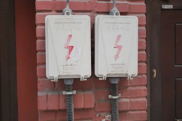 Two electrical boxes with lightning bolt on brick wall.
