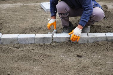 Yeni bir kaldırım inşa etmek için birbirlerine beton tuğla döşeyen bir işçi..