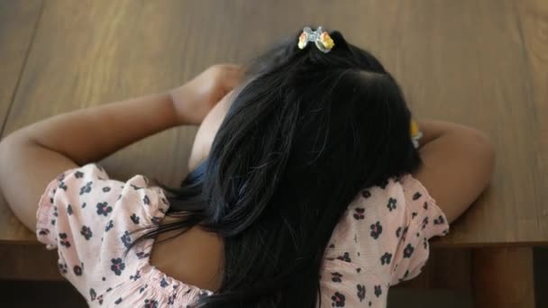 小さな女の子がテーブルに座って 頭が彼女の手の上に休んでいる — ストック動画