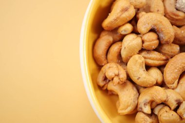 Sarı arka planda küçük bir kasede kaju fıstığı. ,