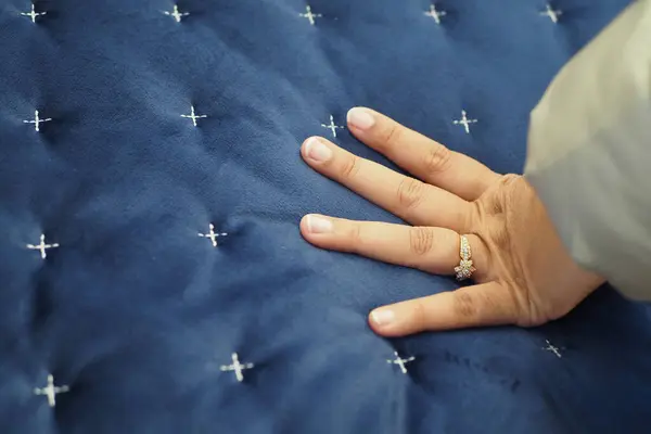 Hand touching and pressing orthopedic mattress on bed