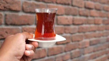 Geleneksel Türk çayını tuğla duvara dayamış bir kadın. .