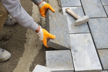 Yeni bir kaldırım inşa etmek için birbirlerine beton tuğla döşeyen bir işçi..