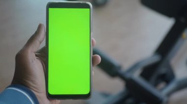 Adam spor salonunda yeşil ekran akıllı telefonu tutuyor..